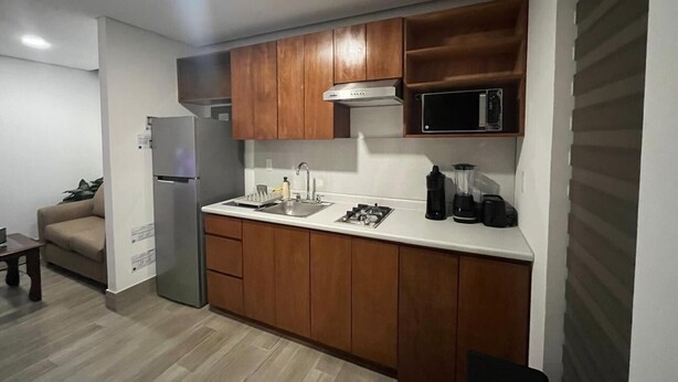 A compact kitchen with wooden cabinets, a stainless steel refrigerator, a microwave, and a gas stove. - Patriota Loft for 2, with amenities and parking (Monterrey)