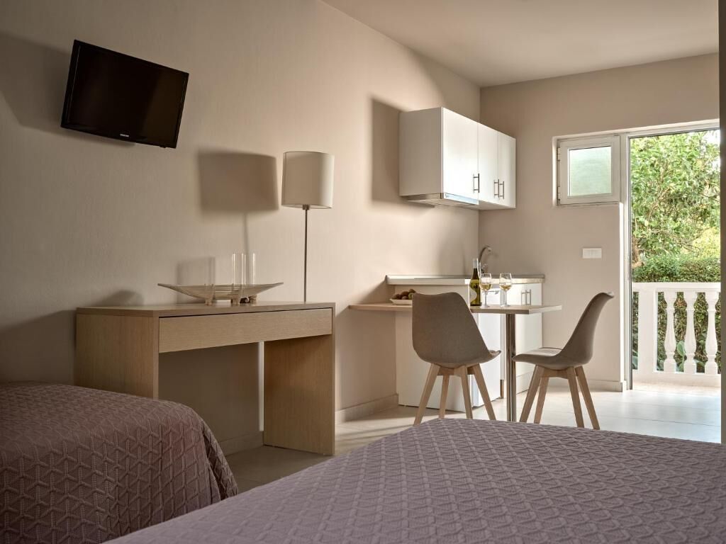 Quarto com cama, escrivaninha com cadeira, televisão na parede e varanda com guarda-corpo.