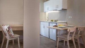 A modern kitchen with white cabinets, a dining table with chairs, and a small refrigerator. - Katerina Studios (Planos)