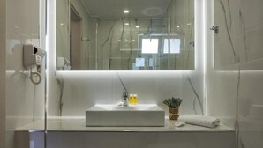 A bathroom with a white sink, a mirror, a handheld showerhead, and a towel. - Katerina Studios (Planos)
