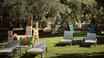 A park with lounge chairs, a slide, and a large tree.