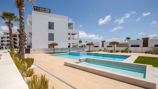 Un hotel moderno con piscina, palme e un cielo azzurro intenso.