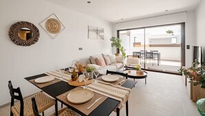 Un soggiorno moderno con zona pranzo, un divano e un'ampia porta scorrevole in vetro che dà su un balcone.