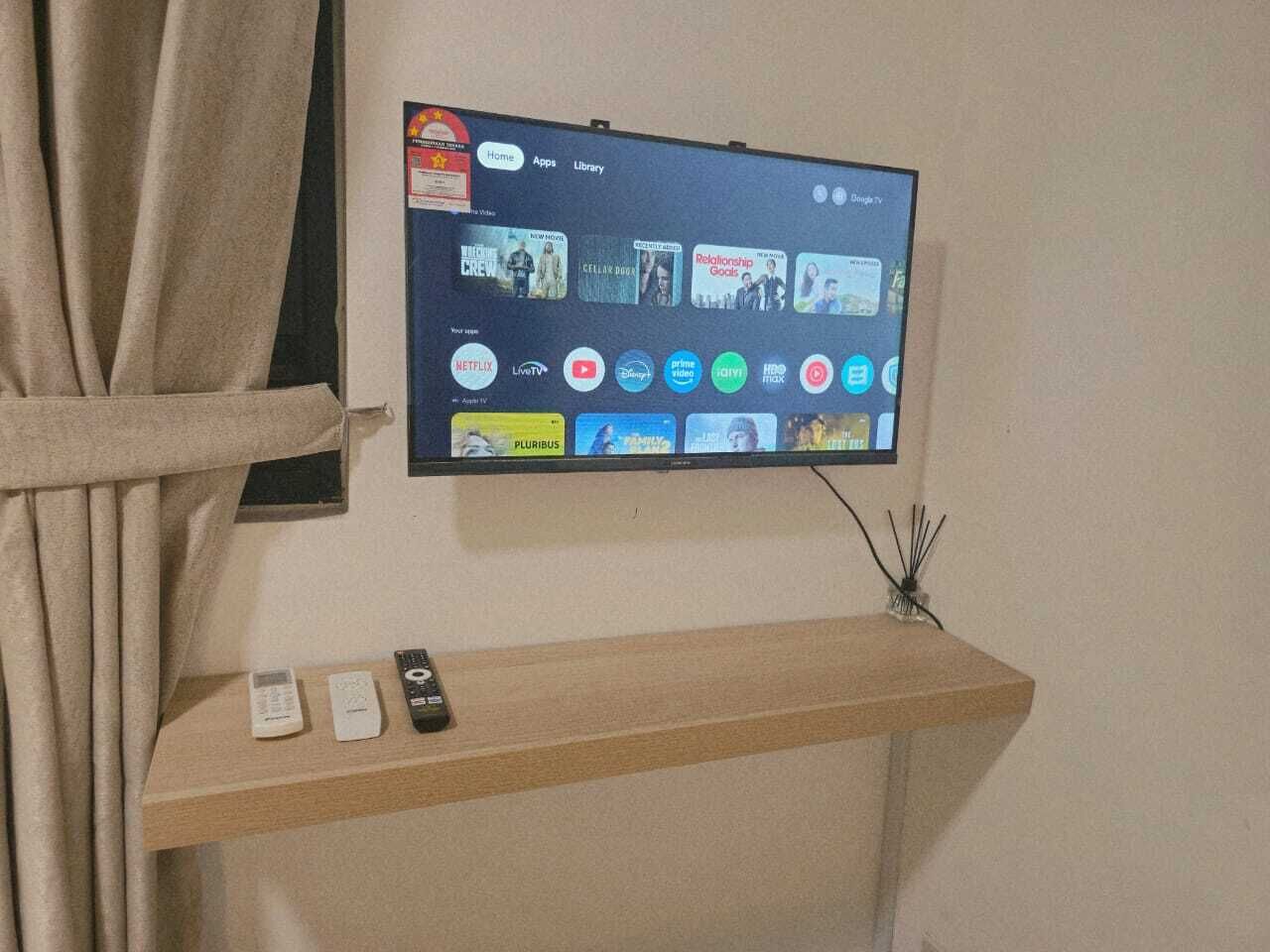 Un televisor montado en la pared con un estante de madera debajo que muestra controles remotos.