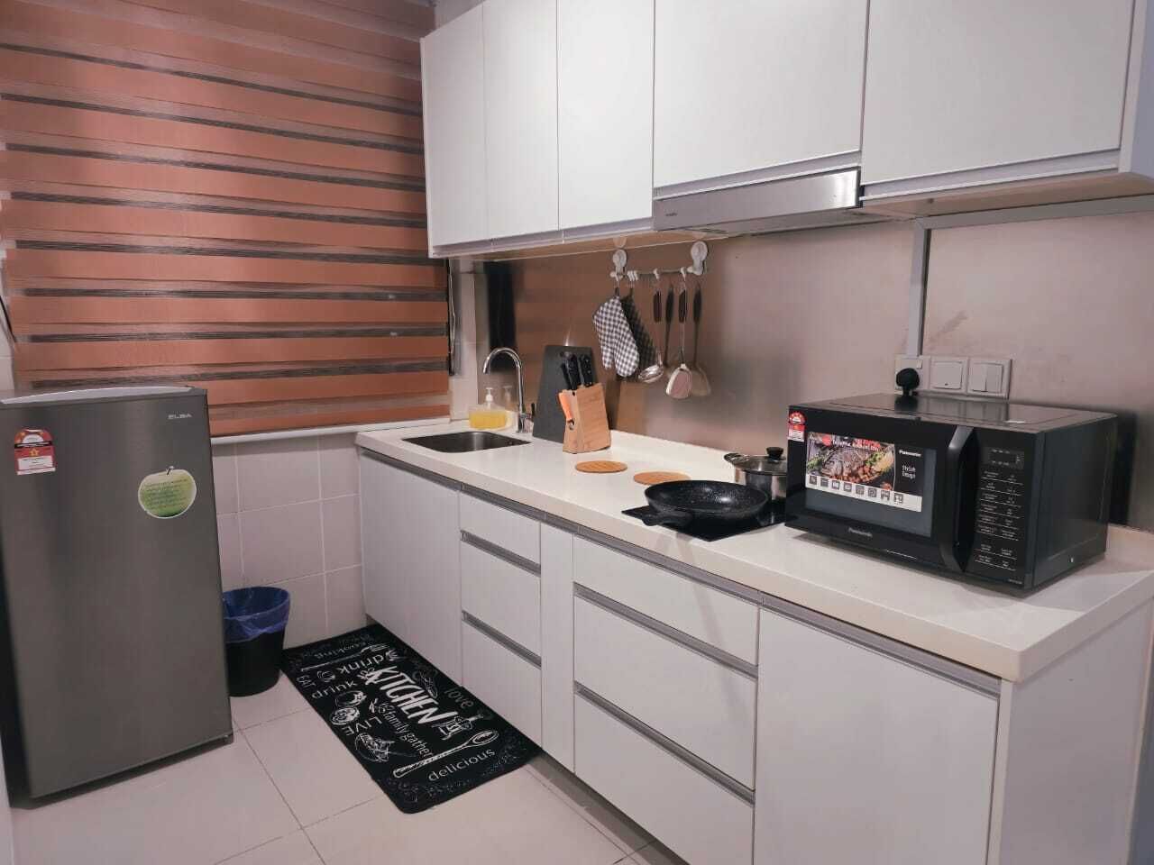 Una cocina compacta con refrigerador, microondas, pileta y un tapete negro con texto.