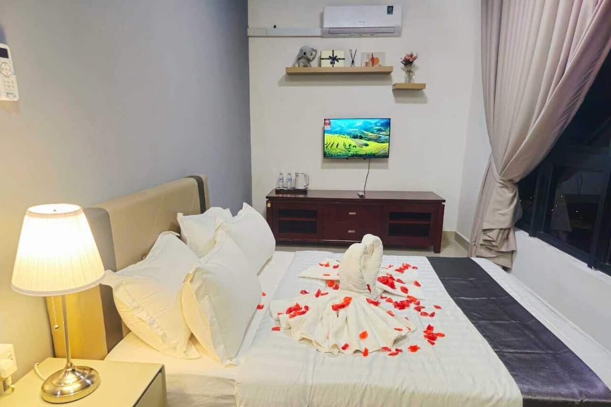 A hotel room with a bed, a bedside lamp, a TV on the wall, and a window with curtains.