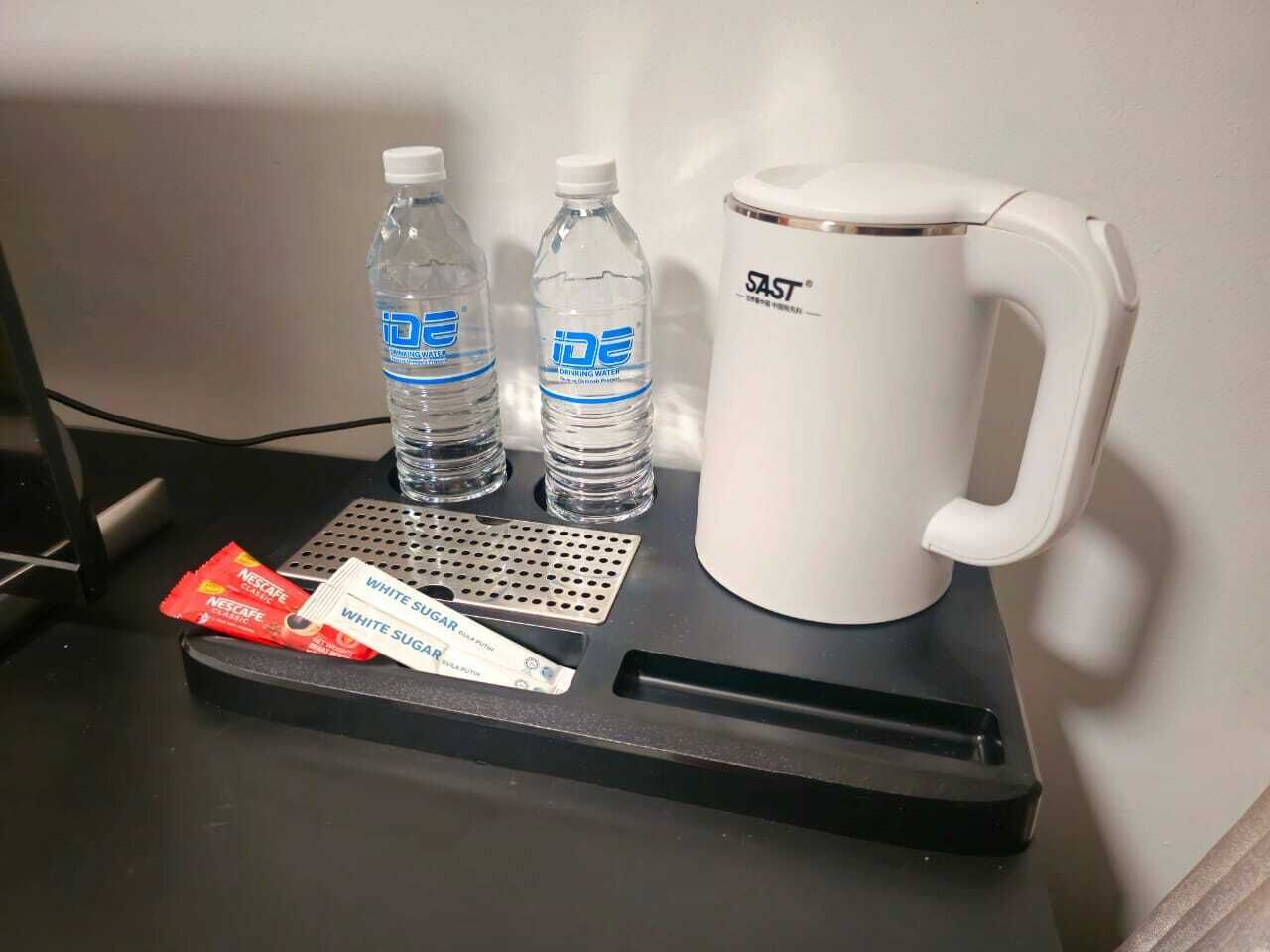 Una bandeja con una taza blanca, dos botellas de agua y sobres de azúcar blanco y café Nespresso sobre una mesa.