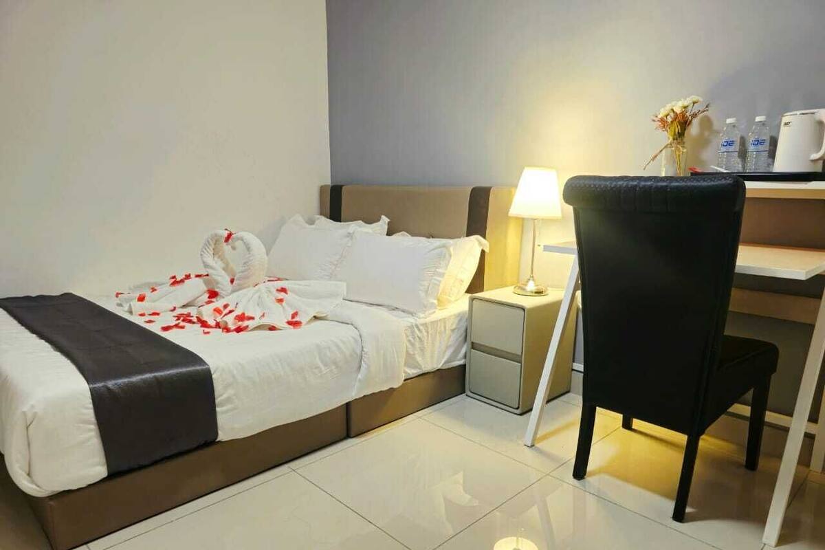 A hotel room with a bed, bedside table, lamp, chair, and a desk with a vase of flowers.