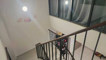 A staircase with a metal railing leading to a room with a window, a radiator, and a small table with items on it.