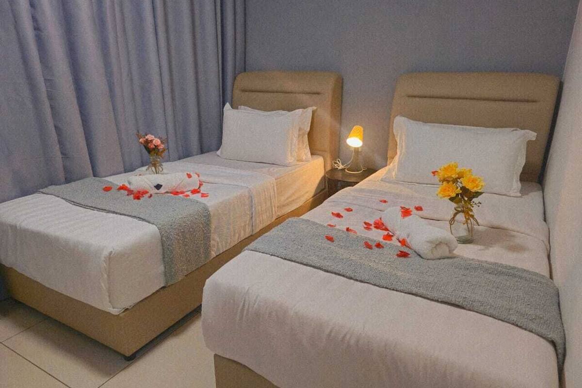 Two twin beds with white linens, a nightstand with a lamp, and a vase with flowers.
