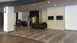 Eine großzügige Lobby mit einer Rezeption, einer Sitzecke und einer Treppe zu einem Aufzug.
