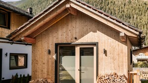 Une cabane en bois dotée d’une grande porte-fenêtre coulissante, d’un toit en pente et d’une pile de bois de chauffage à l’extérieur.