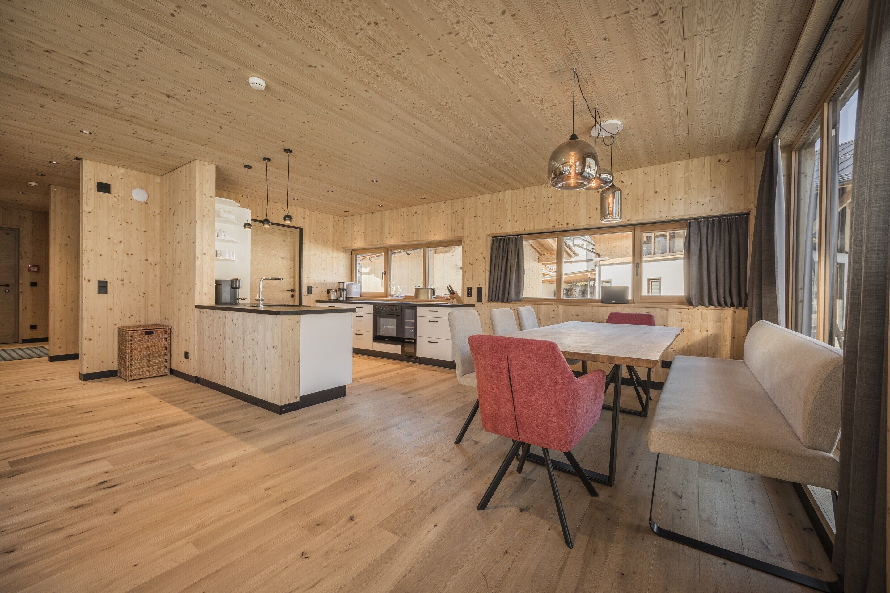 A spacious kitchen with wooden cabinetry and a central island, a dining area with a table and chairs, and large windows providing natural light.