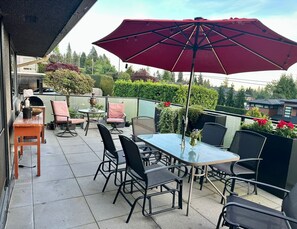 Eine Terrasse im Freien mit Tisch und Stühlen, einem roten Sonnenschirm und Blick auf die Umgebung.