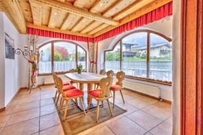 Ein Essbereich mit Holztisch und -stühlen, großen Fenstern und Blick ins Freie.