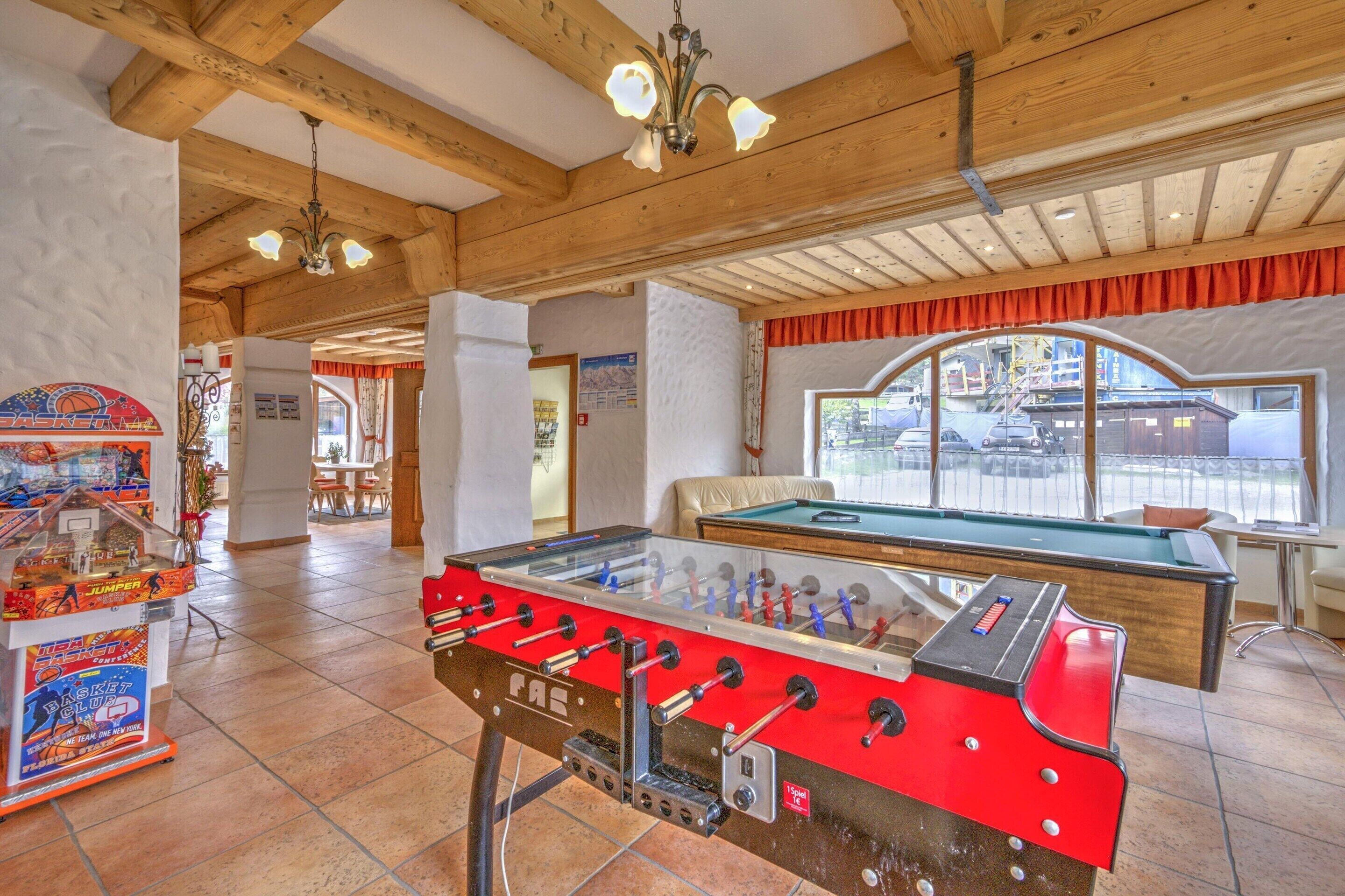 A room with a foosball table, a pool table, and a basketball arcade.