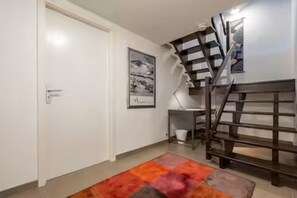 Een gang met een witte deur, een trap en een ingelijst schilderij aan de muur.