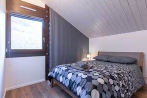 Een slaapkamer met een bed, gordijnen, een raam en een houten plafond.