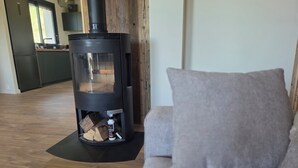 Ein modernes Wohnzimmer mit Kaminofen, einer Couch und einer Küche im Hintergrund.