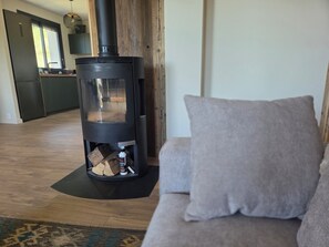 Ein modernes Wohnzimmer mit Kaminofen, einer Couch und einer Küche im Hintergrund.