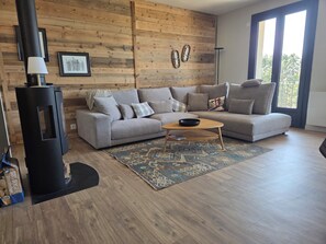 Un salon moderne avec un canapé d’angle, un poêle à bois noir et une grande fenêtre.