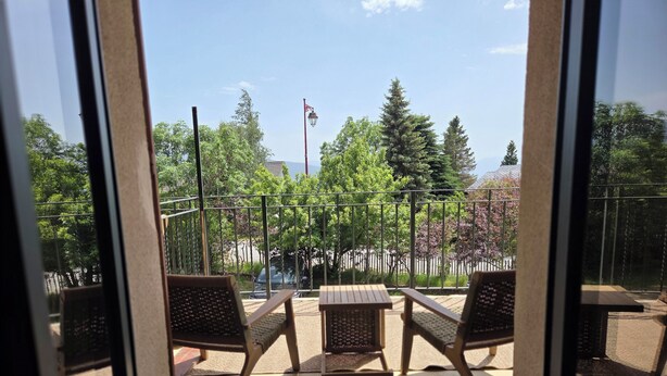 Ein Balkon mit zwei Stühlen, einem Tisch, einem Metallgeländer und Bäumen im Hintergrund.