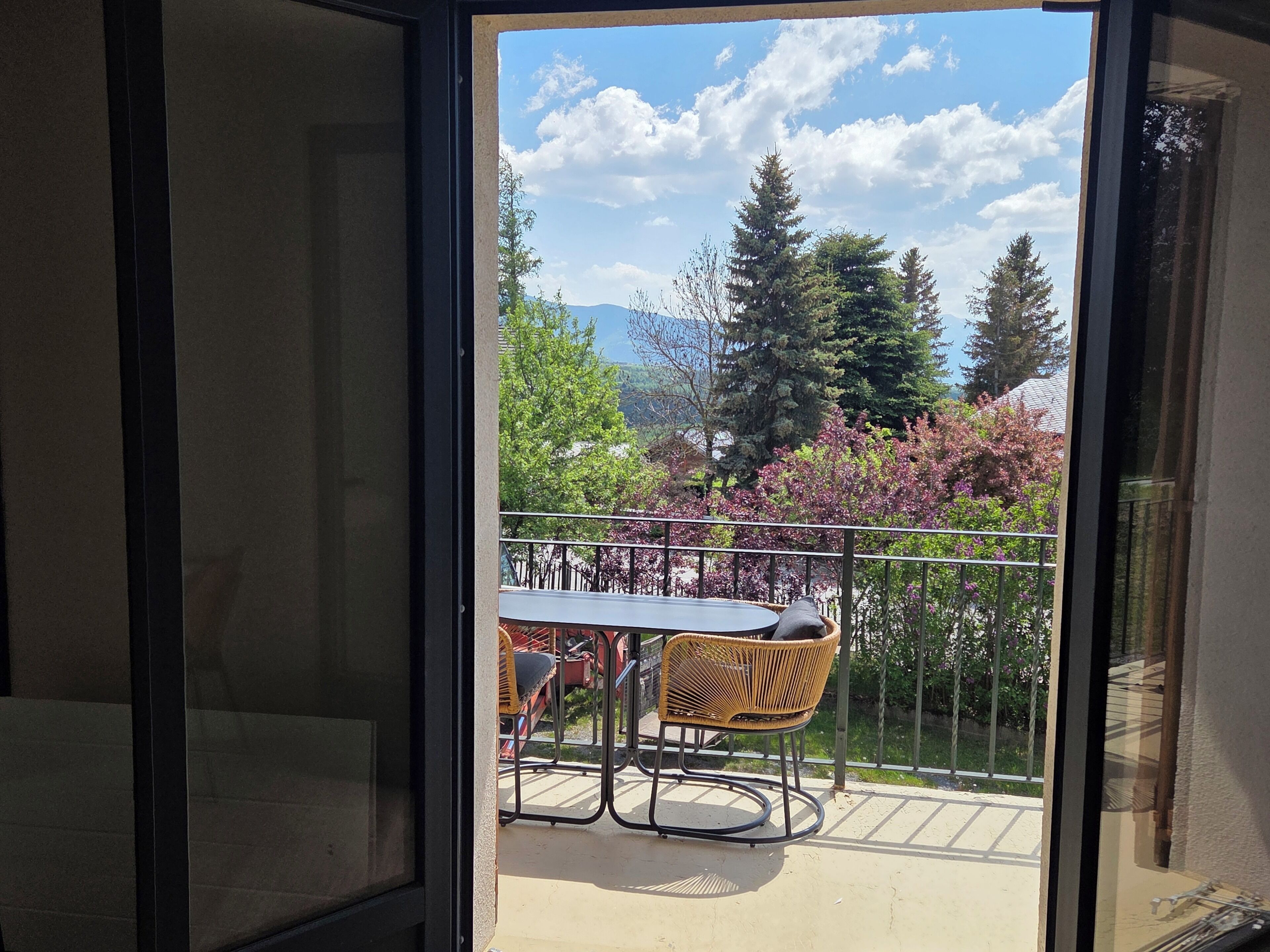 Un balcon avec une table et des chaises, une balustrade et une vue sur les arbres et les montagnes.
