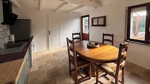 A dining area with a wooden table and chairs, a kitchen with a stove and sink, and a window with a view of the outdoors.