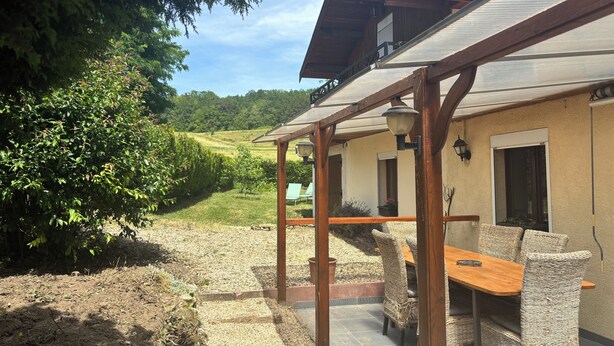 A covered patio area with wicker furniture and a table, overlooking a vineyard.