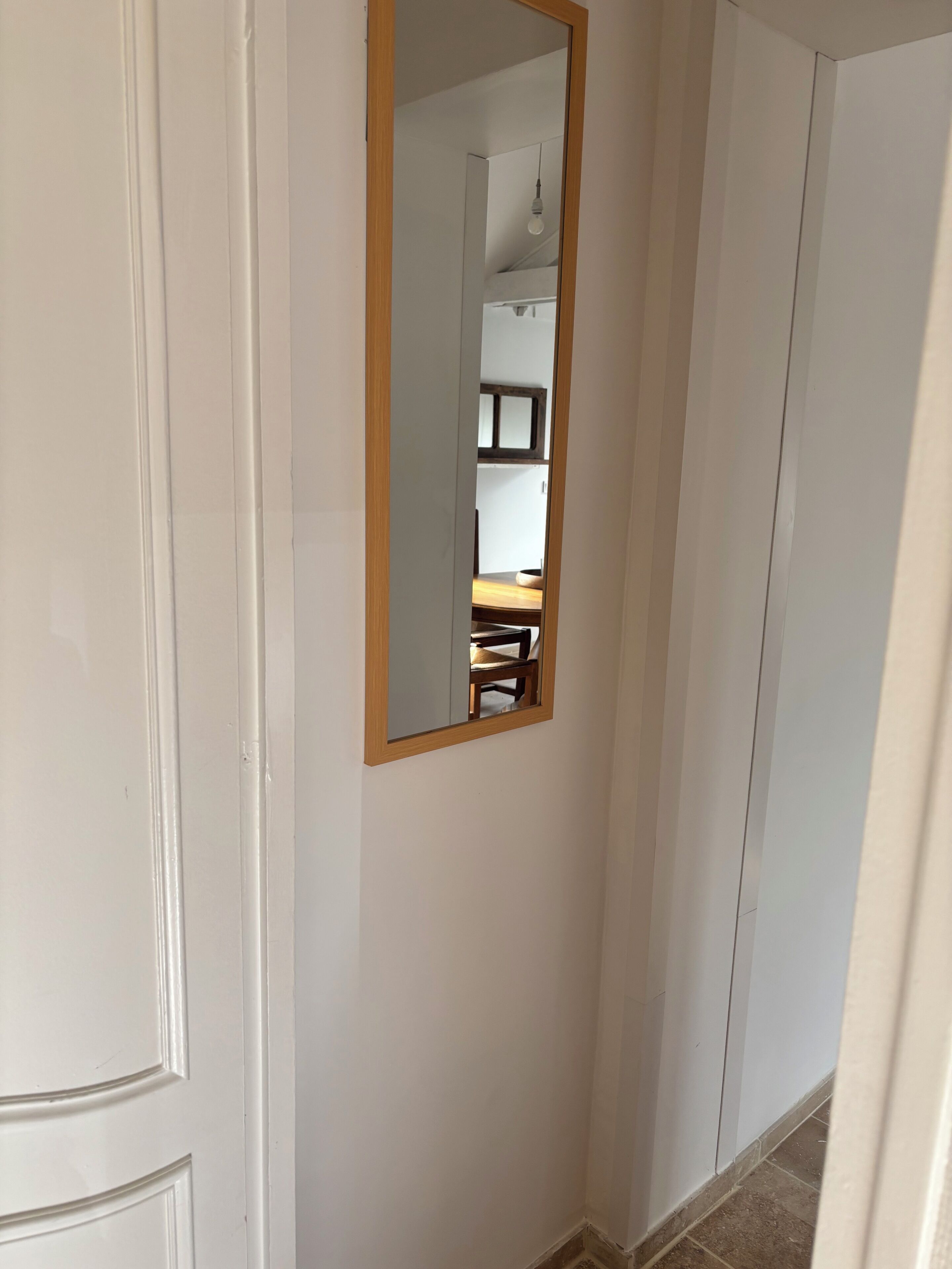 A white door with a wooden-framed mirror reflecting a room with a chair and a table.