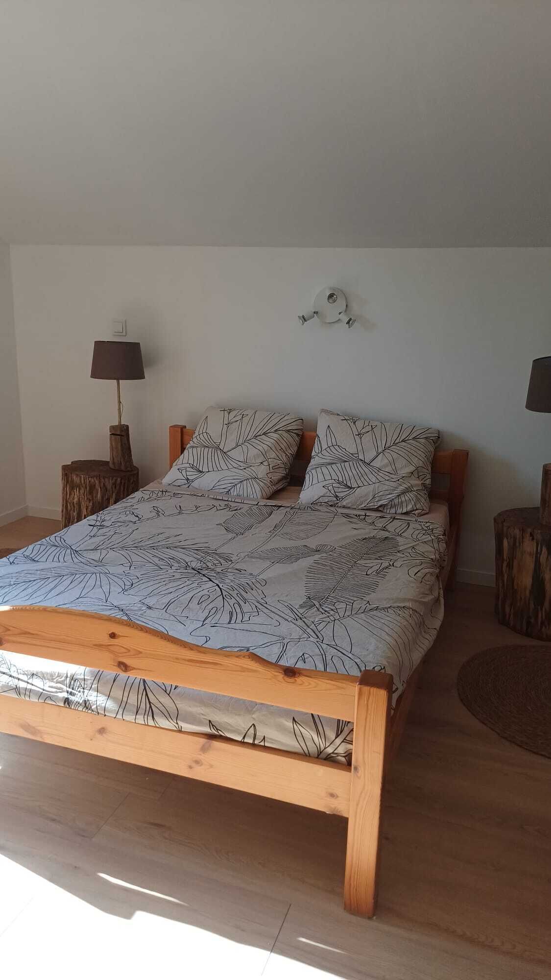 A wooden bed with a leaf-patterned bedspread, two nightstands with lamps, and a wall-mounted light fixture.