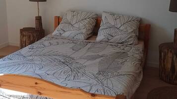 A wooden bed with a leaf-patterned bedspread, two nightstands with lamps, and a wall-mounted light fixture.