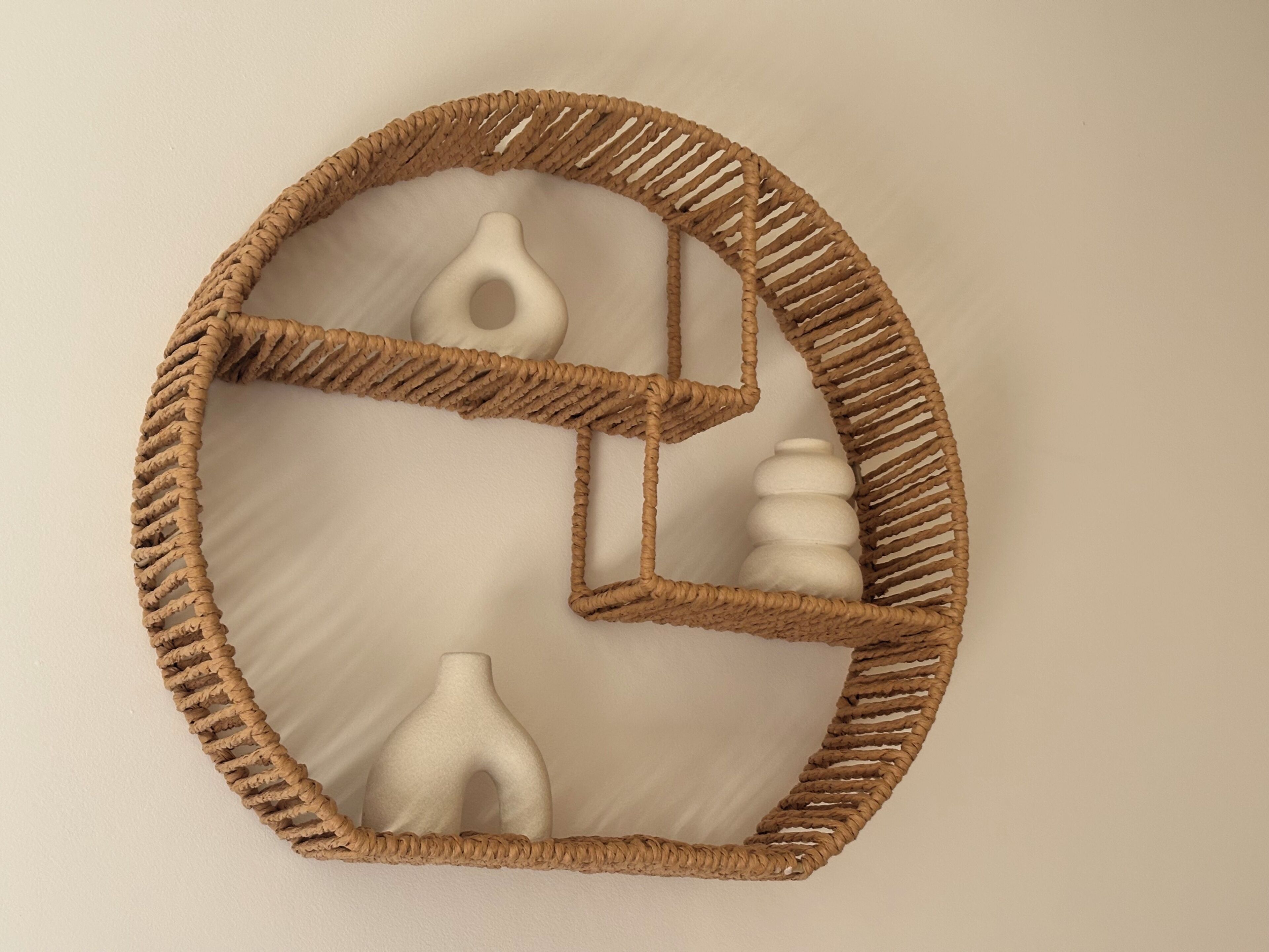 Une étagère tissée fixée au mur, sur laquelle reposent trois objets en céramique blanche.