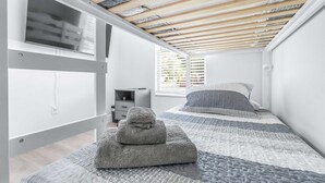 Un dormitorio con techo inclinado, una cama con colcha estampada, una mesita de noche y una ventana con persianas.