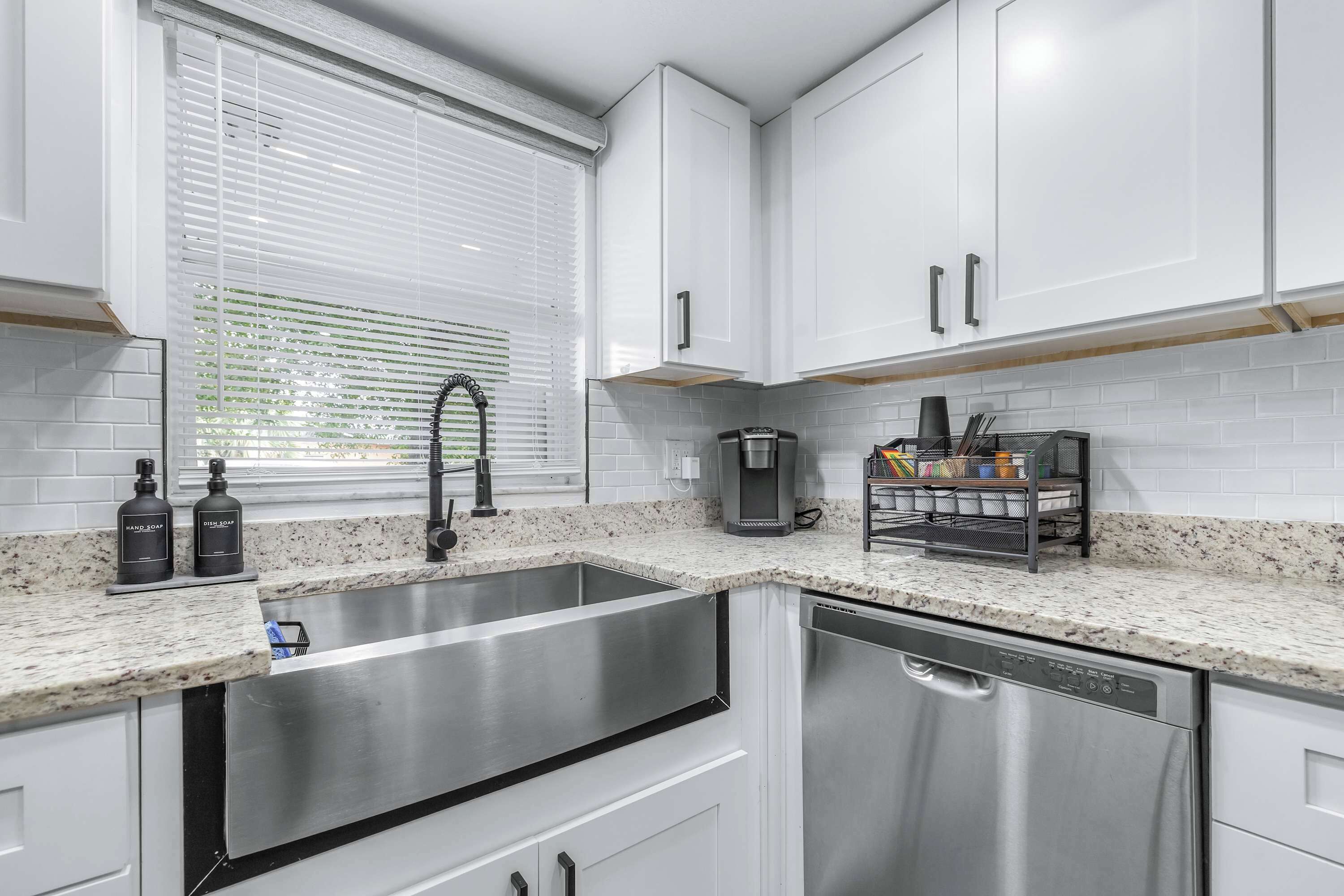 A modern kitchen with white cabinets, stainless steel appliances, a double sink, and a coffee maker.