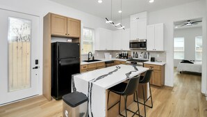 A modern kitchen with a central island, wooden cabinets, and a black refrigerator. - Luxury Retreat - 5 Min to NRG & Med Center - Sleeps 8 - Backyard + Free Parking (Houston)