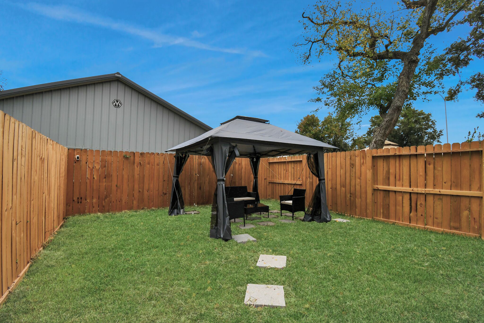 A backyard with a wooden fence, a gazebo, and a shed.