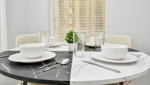 A dining table set with white plates, bowls, cutlery, and glasses, with a potted plant and a window with blinds in the background. - Luxury Retreat - 5 Min to NRG & Med Center - Sleeps 8 - Backyard + Free Parking (Houston)