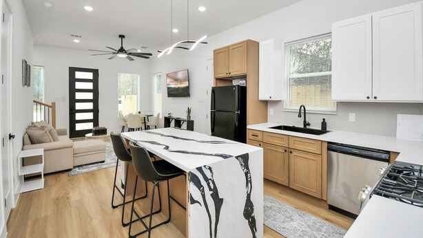 A modern kitchen with a central island, wooden cabinets, a black refrigerator, and a dining area with a sofa and chairs. - Luxury Retreat - 5 Min to NRG & Med Center - Sleeps 8 - Backyard + Free Parking (Houston)