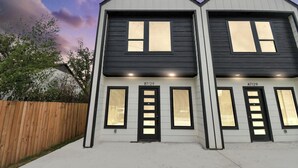 A two-story building with a symmetrical facade, numbered B7129 and A7129, featuring a central door flanked by windows and a wooden fence in the background. - Luxury Retreat - 5 Min to NRG & Med Center - Sleeps 8 - Backyard + Free Parking (Houston)