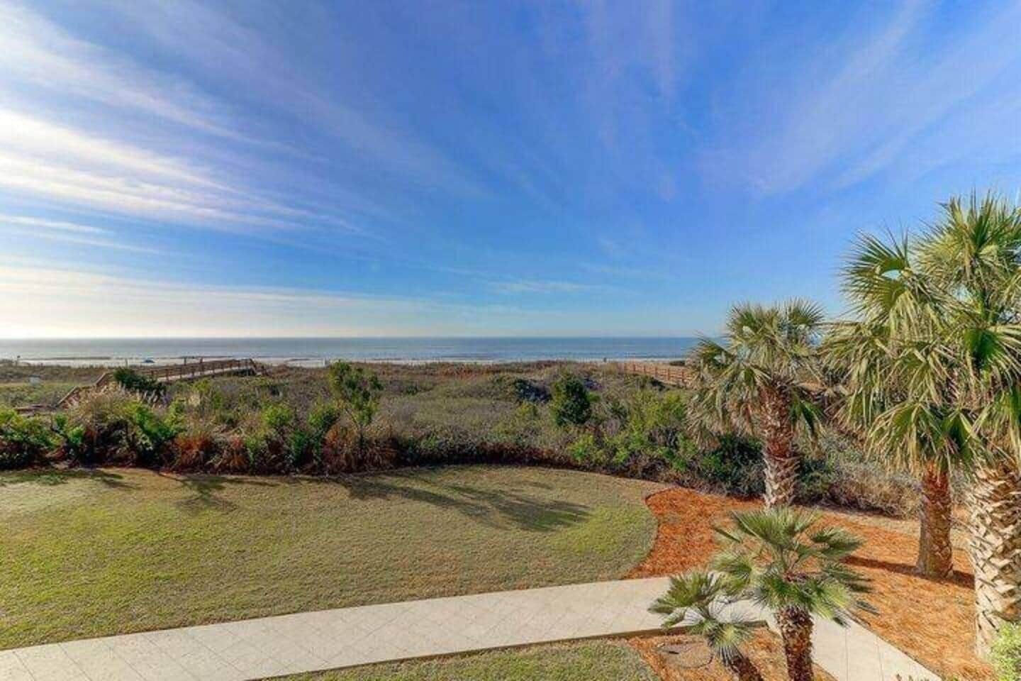 A coastal landscape with a paved pathway, palm trees, and a view of the ocean.