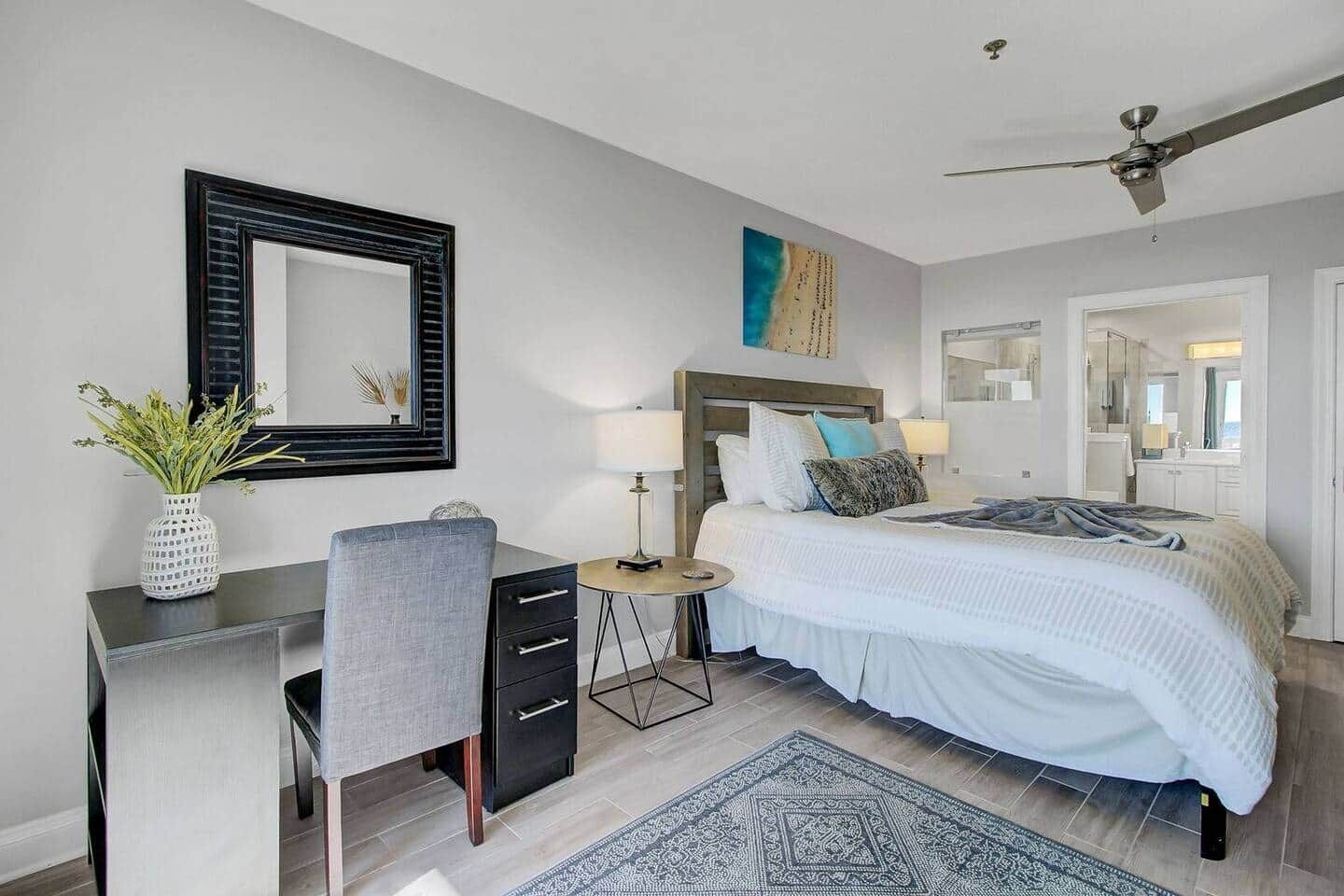 A bedroom with a bed, desk, chair, and a mirror.