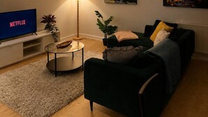 A living room with a TV, a lamp, a sofa, and two paintings on the wall. - Spacious 2 Bed apartment Rainham LDN Gated Parking (Greater London)