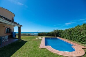 Ein Pool mit Backsteinrand, eine Terrasse mit Tisch und Stühlen und Blick aufs Meer.