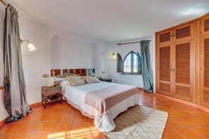 Ein Schlafzimmer mit Bett, Nachttisch, Lampe, Fenster und einem Holzschrank.