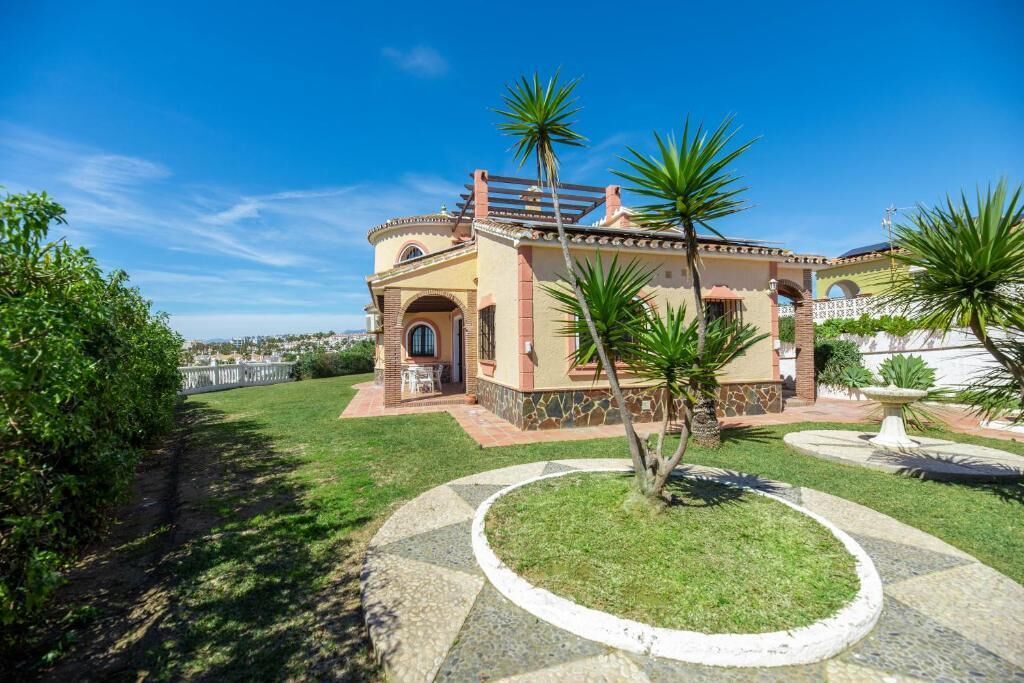 A house with a circular driveway, a patio, and a small garden with palm trees.