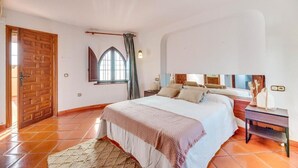 A bedroom with a bed, a nightstand, a window with curtains, a wooden door, and a tiled floor. - LXR Villa Sirena Oceanfront 3-Bedroom (El Faro)