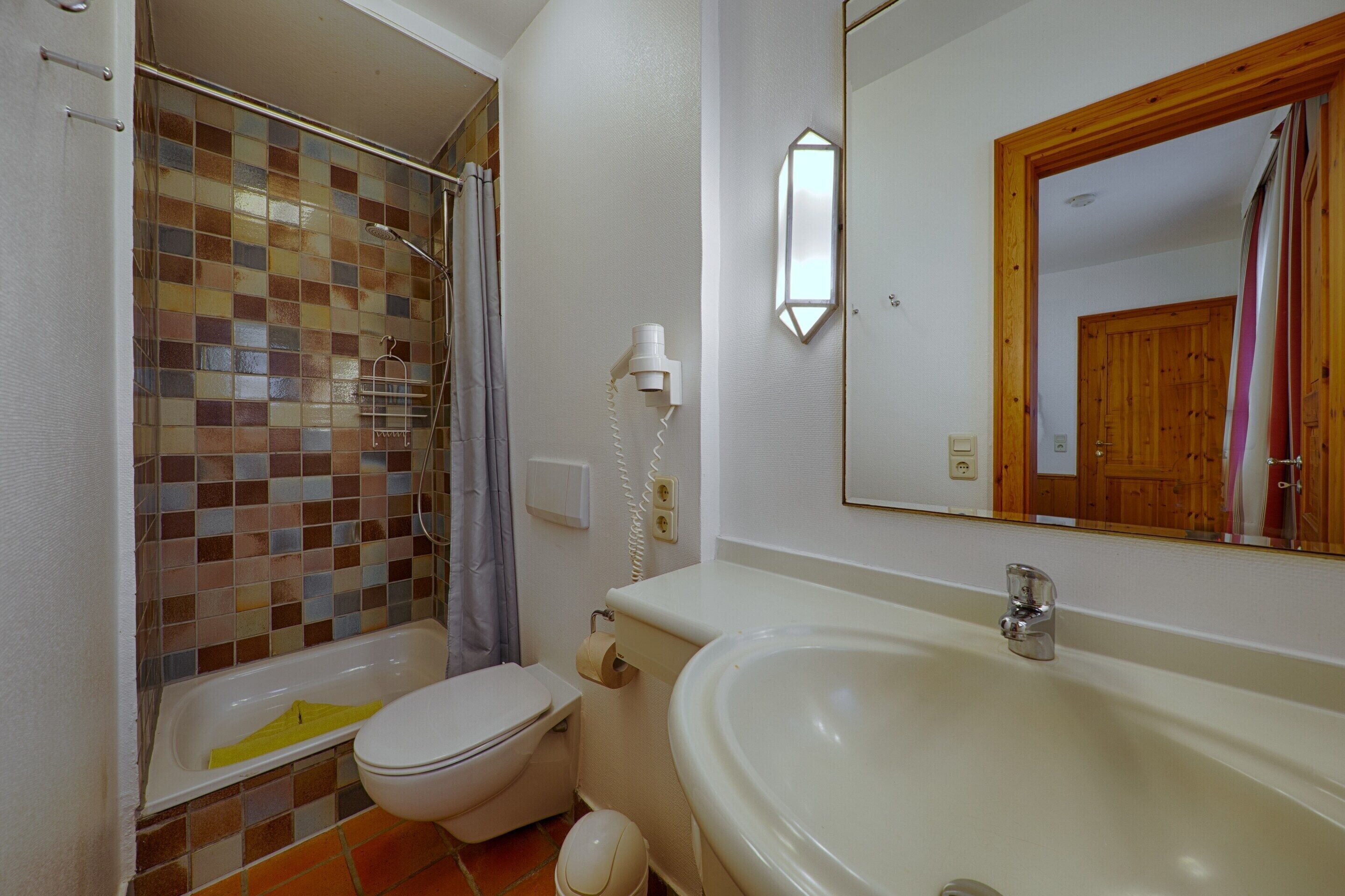 A bathroom with a shower, toilet, sink, and a mirror.