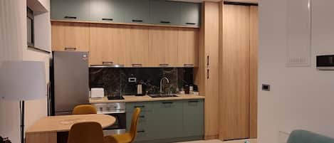 A compact kitchen with wooden cabinets, a dining table with chairs, and a sofa with a colorful pillow.