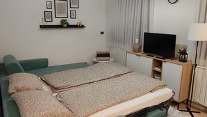Un dormitorio moderno con un sofá cama verde, un televisor de pantalla plana, un reloj y una estantería con cuadros enmarcados.